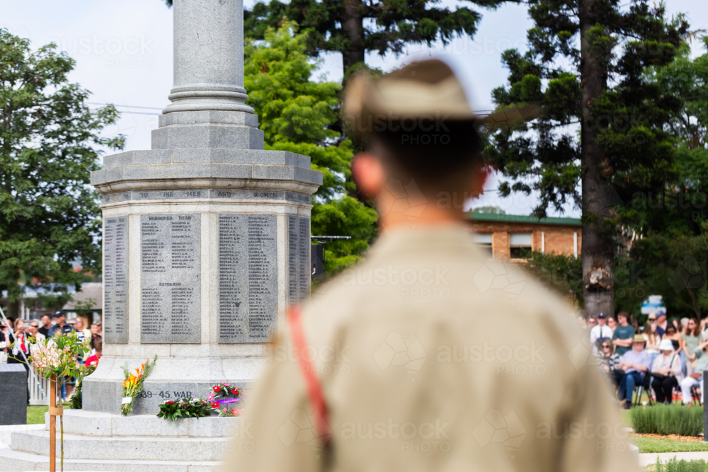 ANZAC day memorial service with focus on cenotaph and blurred soldier in foreground - Australian Stock Image
