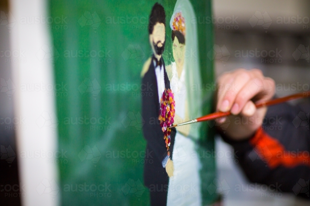 Artist adding paint to painting of a married couple on canvas - Australian Stock Image