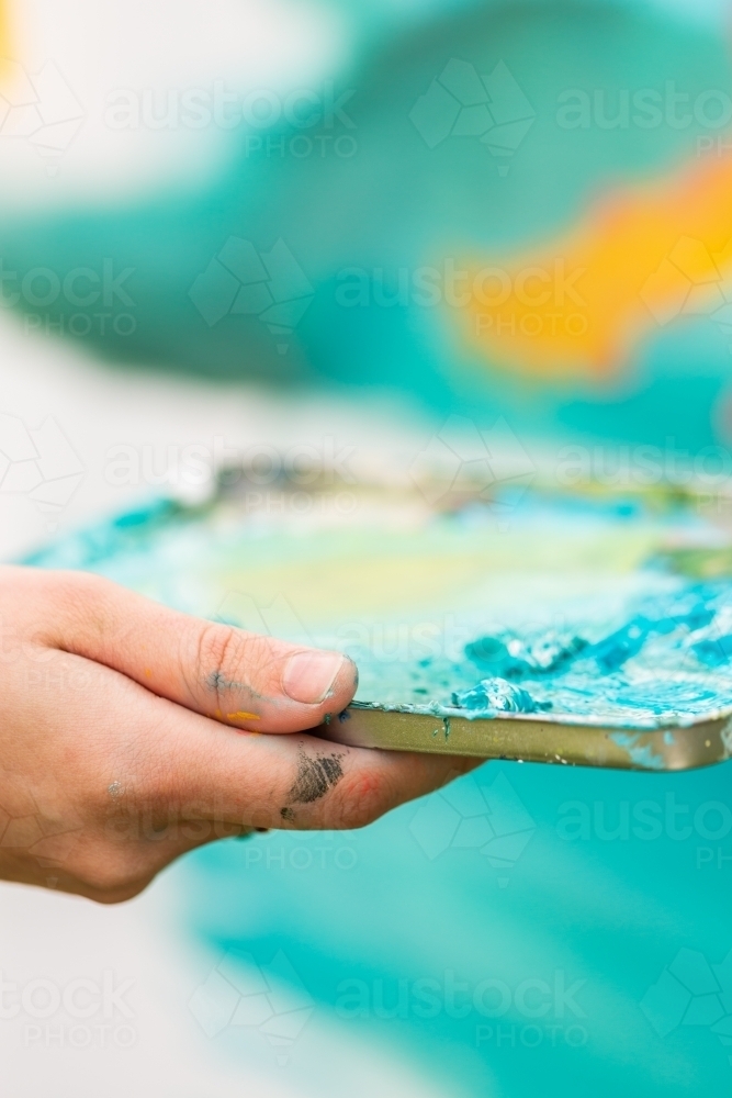 Artist holding messy paint pallet tray for mixing colours - Australian Stock Image