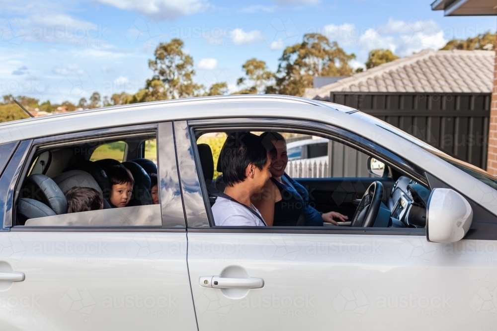 Asian Australian man driving his family in car reversing out driveway of home - Australian Stock Image