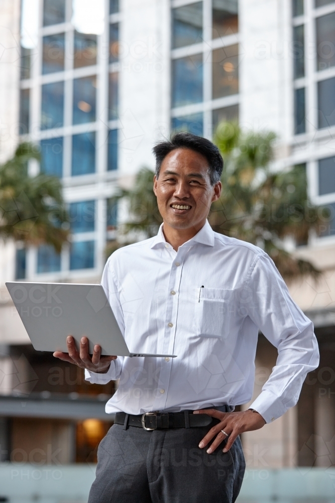 Asian businessman holding laptop in city - Australian Stock Image