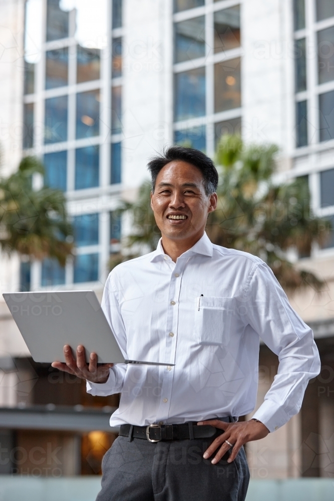 Asian businessman holding laptop in city - Australian Stock Image