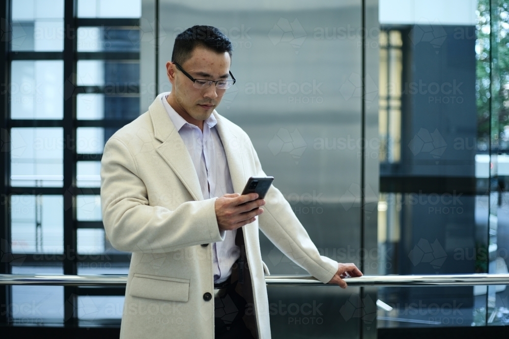 Asian businessman wearing cream coat in modern workplace - Australian Stock Image
