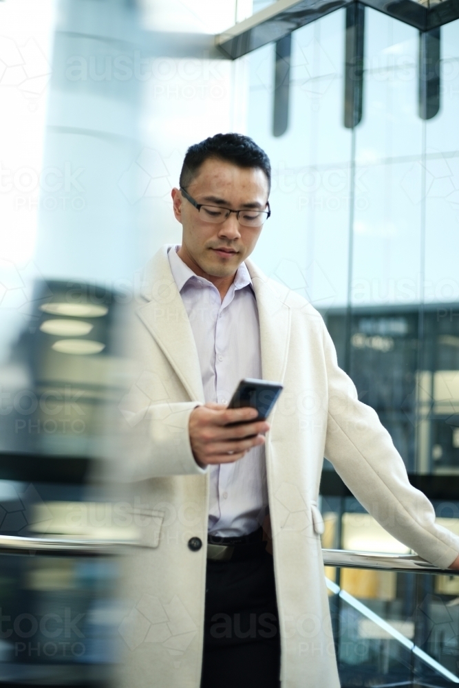 Asian businessman wearing cream coat in modern workplace - Australian Stock Image