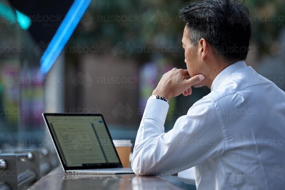 Asian businessman working on laptop in a cafe in the city - Australian Stock Image