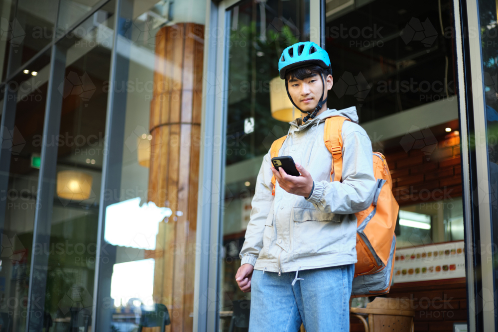 Asian delivery guy walking out of the restaurant while on his phone. - Australian Stock Image