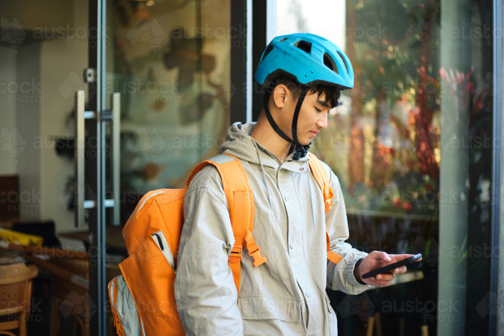 Asian delivery guy walking out of the restaurant while on his phone. - Australian Stock Image