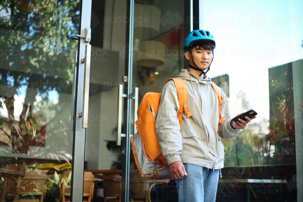 Asian delivery guy walking out of the restaurant while on his phone - Australian Stock Image