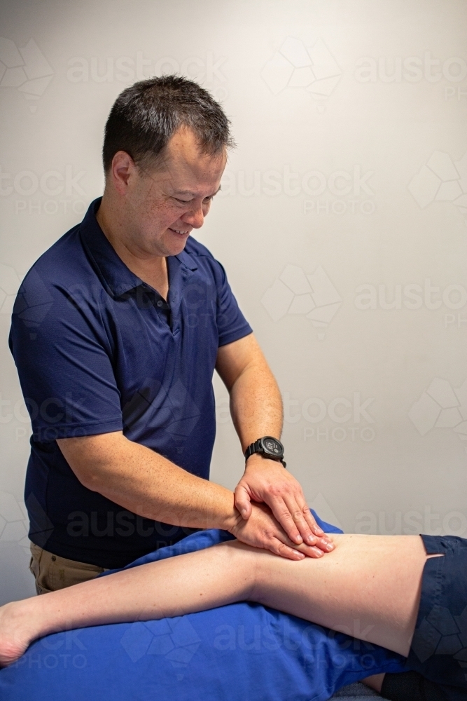 Asian male physio using massage on leg to promote healing - Australian Stock Image