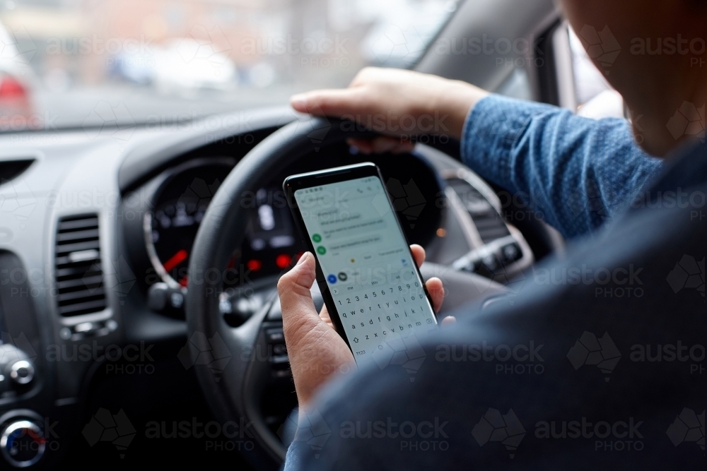 Asian man driving car whilst texting - Australian Stock Image