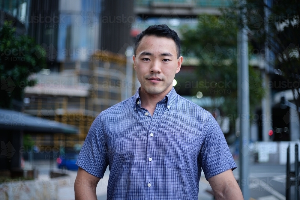 Asian man in blue shirt with city background - Australian Stock Image