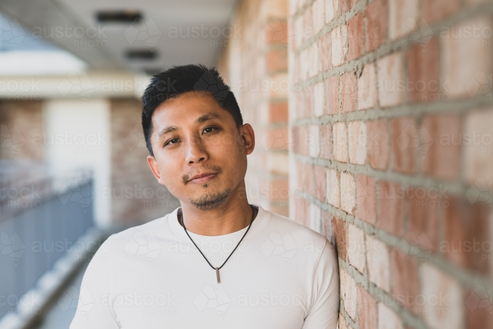 Asian man leaning against the brick wall - Australian Stock Image