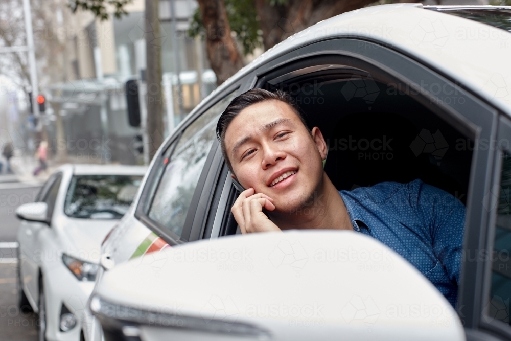 Asian man parked in car talking on mobile phone - Australian Stock Image