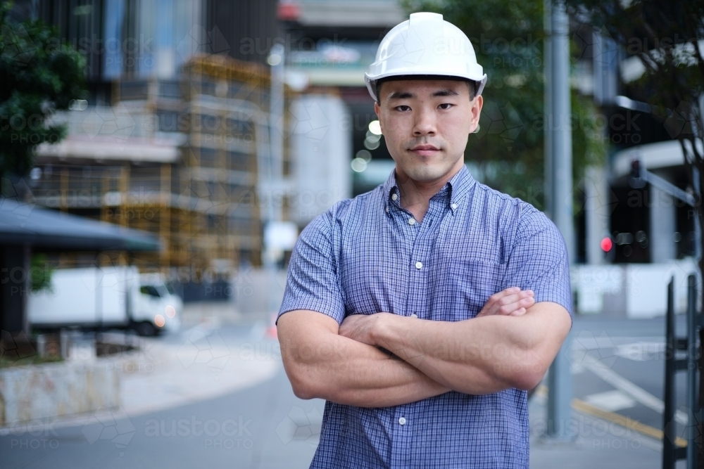 Asian man wearing hard hat with city background - Australian Stock Image