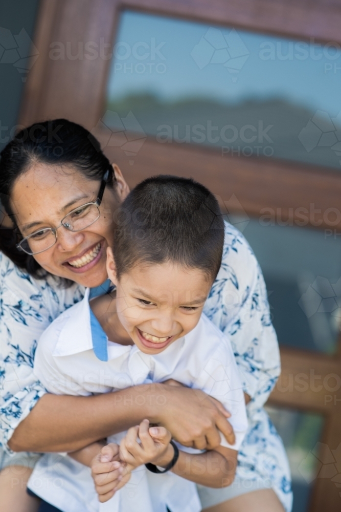 Asian mum hugs her son goodbye at the front door of her home on his first day of school - Australian Stock Image