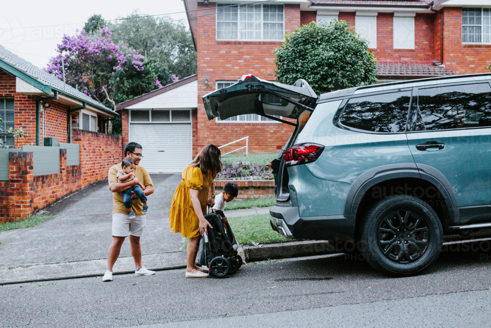 Asian mum loading folded baby stroller into the car boot - Australian Stock Image