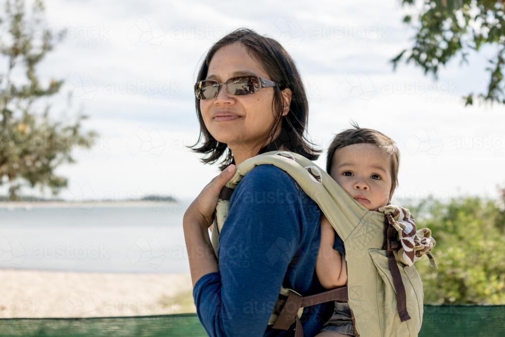 Asian mum outside at the beach walking in the summer sun with her mixed race baby boy - Australian Stock Image