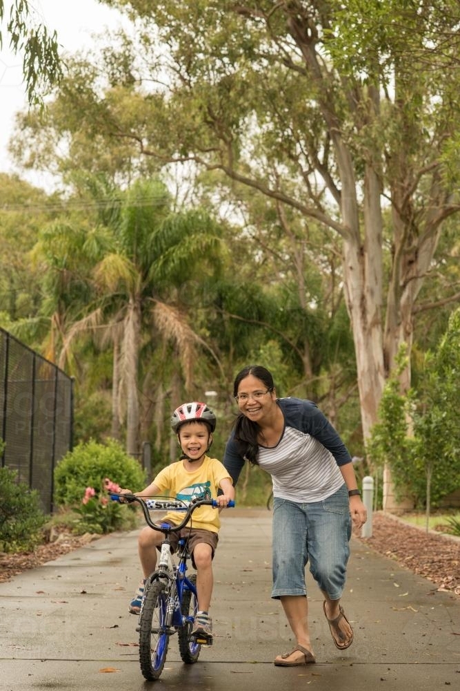Asian mum teaching her mixed race boy to ride a bike - Australian Stock Image