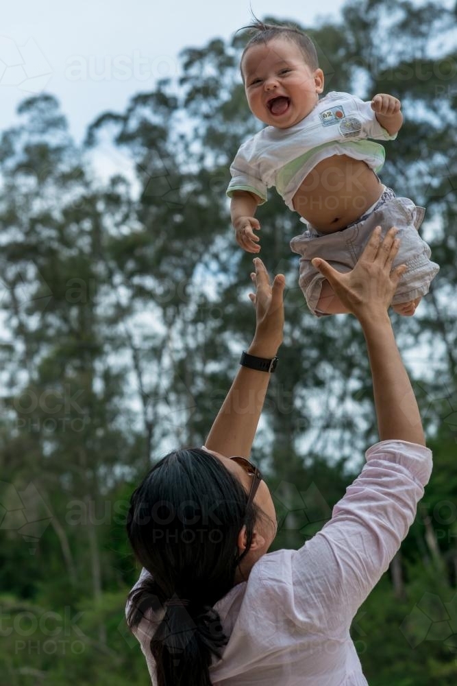 Asian mum throws her baby boy up in the air - Australian Stock Image