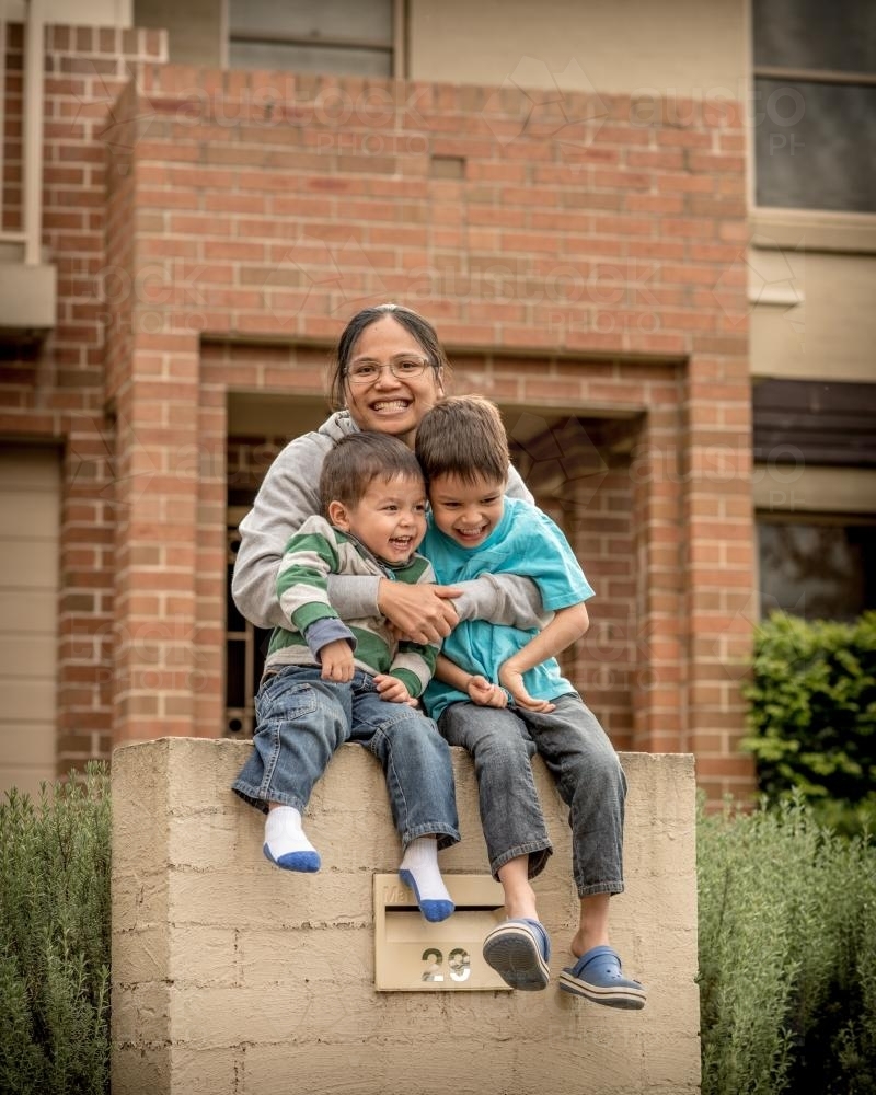 Asian mum with her mixed race boys in front of their suburban home - Australian Stock Image