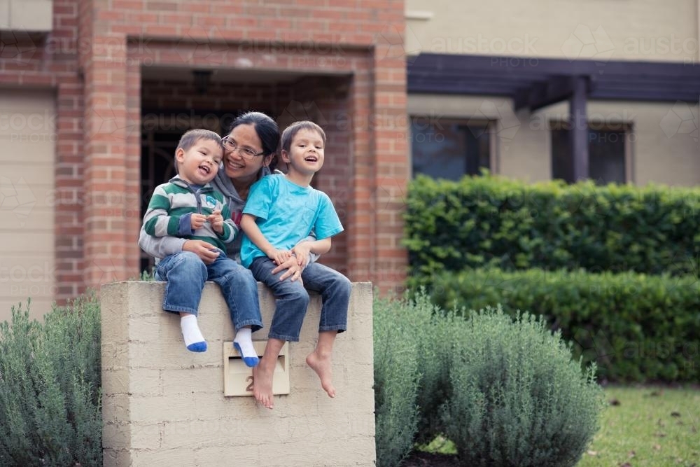 Asian mum with her mixed race boys in front of their suburban home - Australian Stock Image