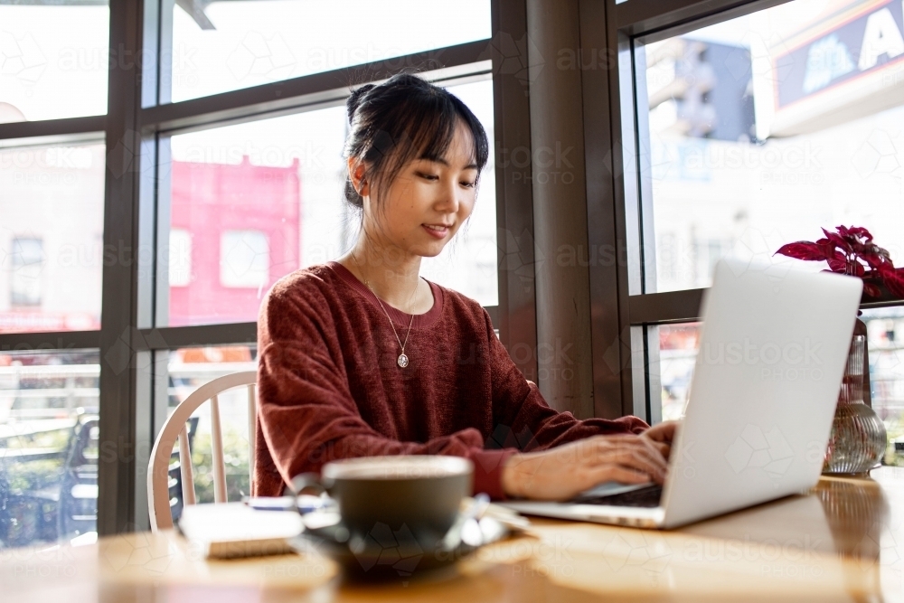 Asian small business owner working remotely on her laptop at a cafe - Australian Stock Image