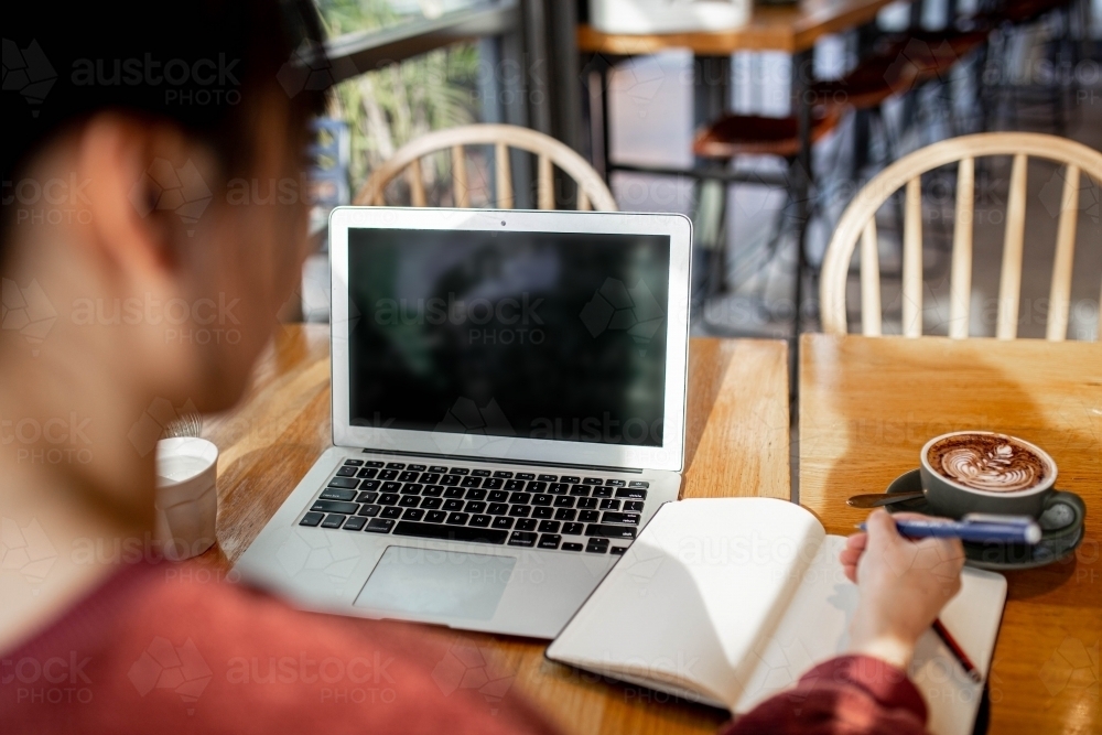 Asian small business owner working remotely on her laptop at a cafe - Australian Stock Image