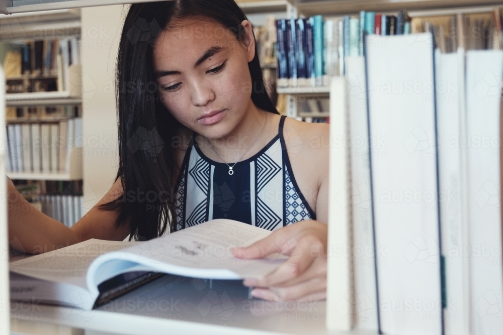 Asian student reading book in university library - Australian Stock Image