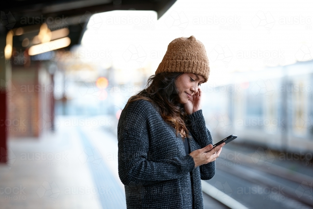 Asian woman checking messages waiting at train station - Australian Stock Image