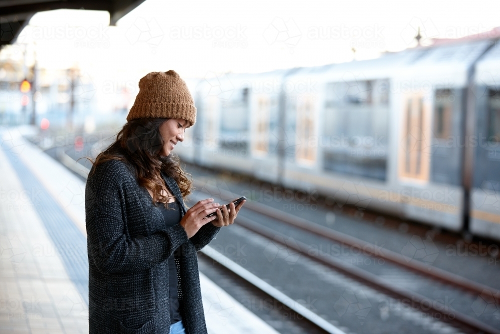 Asian woman checking phone whilst waiting at train station - Australian Stock Image