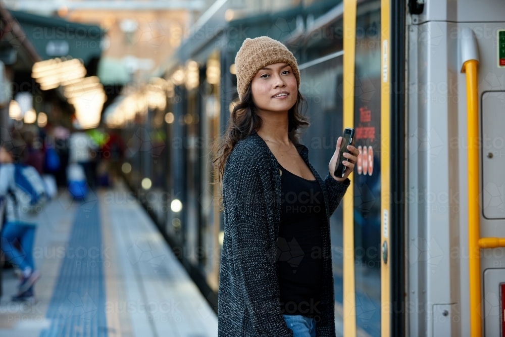 Asian woman getting on train with mobile phone - Australian Stock Image