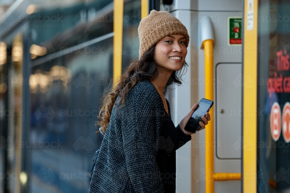 Asian woman getting on train with mobile phone - Australian Stock Image