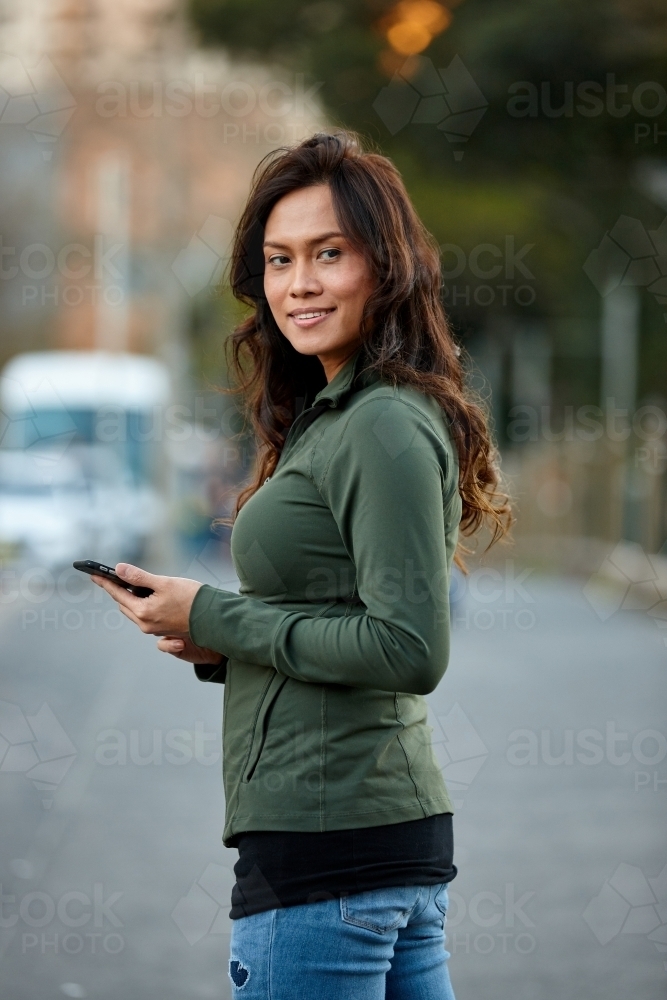 Asian woman hailing taxi with mobile phone - Australian Stock Image