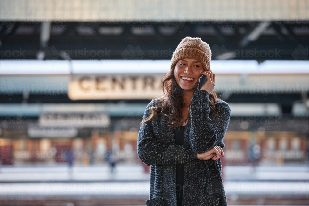 Asian woman laughing whilst talking on mobile at train station - Australian Stock Image