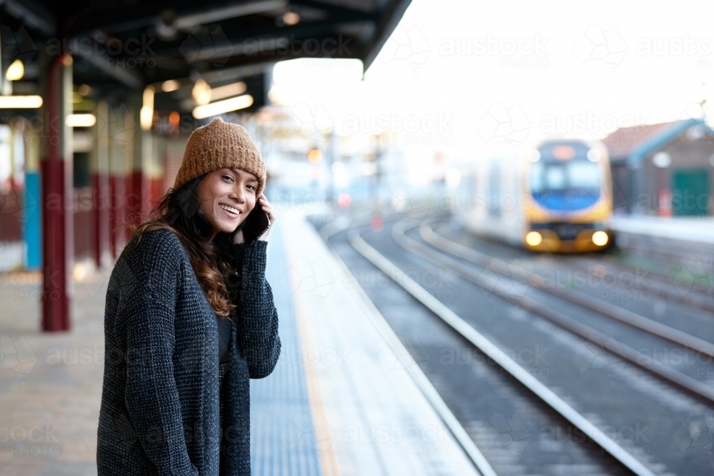 Asian woman laughing whilst waiting at train station with mobile phone - Australian Stock Image