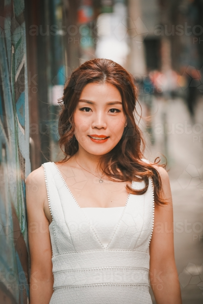 Asian woman leaning against wall in Hosier Lane, iconic graffiti laneway in Melbourne - Australian Stock Image