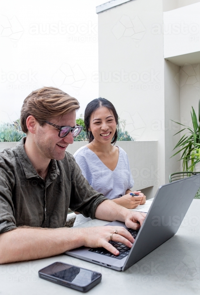 Asian woman working together with a Caucasian man with a laptop at an outdoor office table - Australian Stock Image