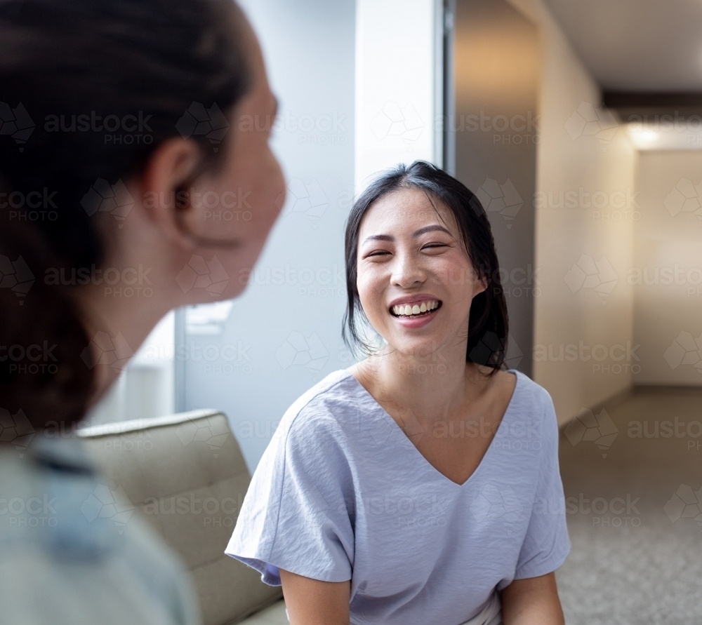 Asian woman smiling while talking to her colleague in an office - Australian Stock Image