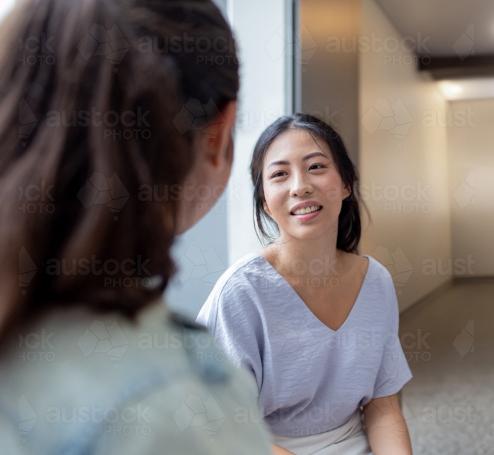 Image of Asian woman smiling while talking to her colleague in an ...