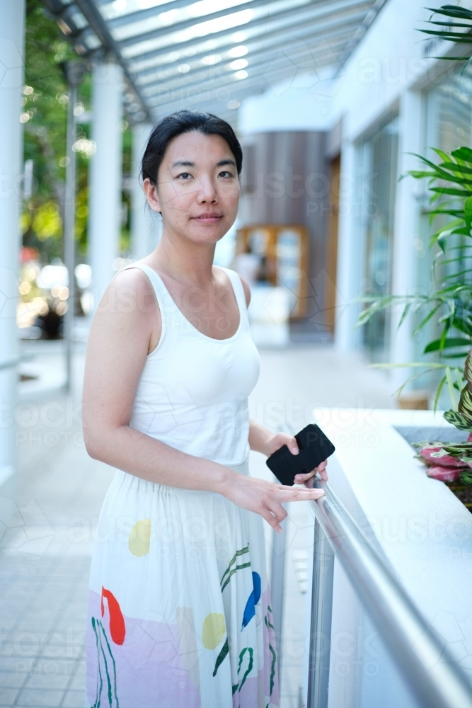 Asian woman standing along the walkway while holding her phone - Australian Stock Image
