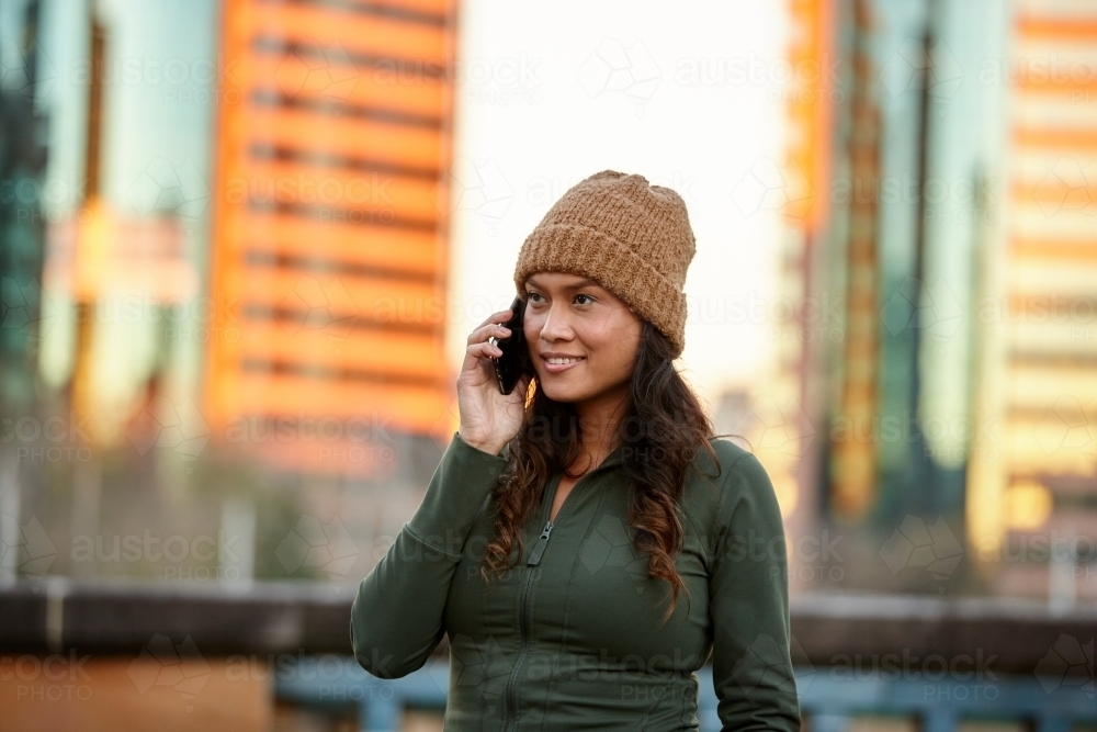 Asian woman talking on mobile phone in city wearing beanie - Australian Stock Image