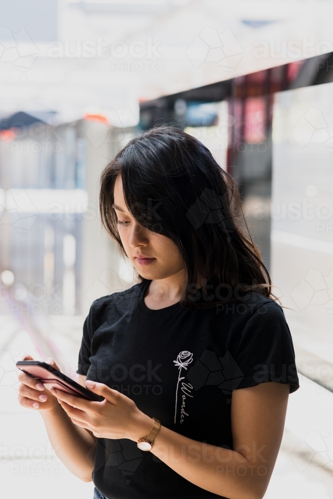 asian woman using phone at train station - Australian Stock Image
