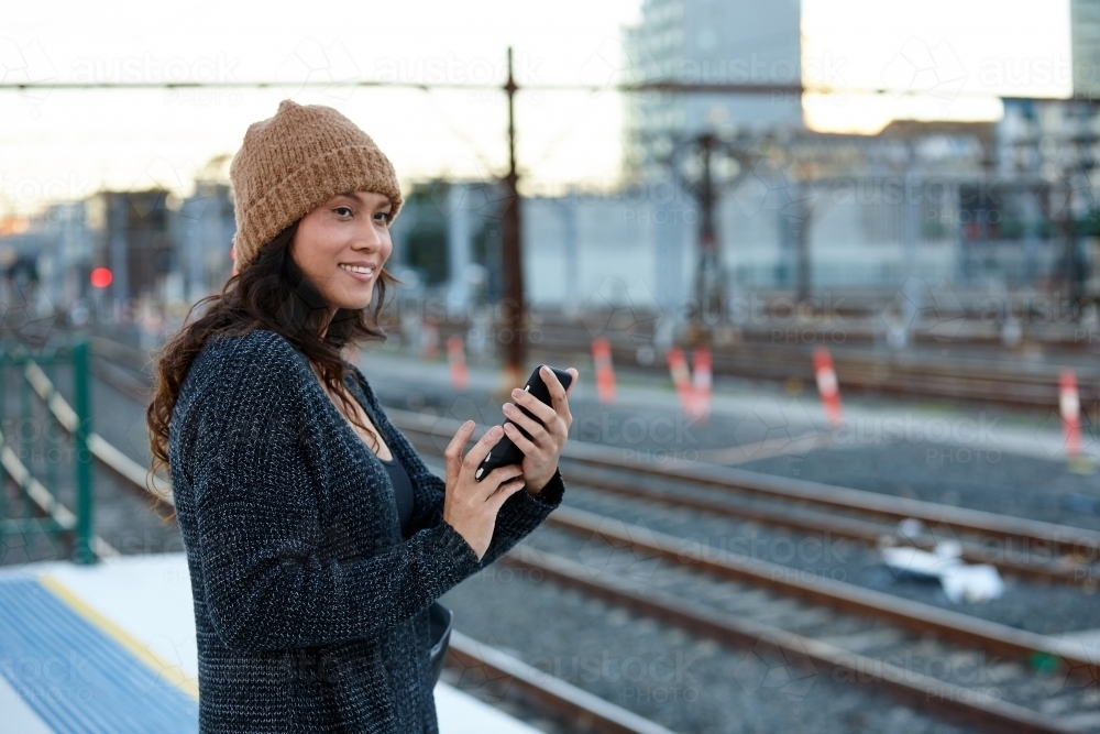 Asian woman waiting at train station holding mobile phone - Australian Stock Image