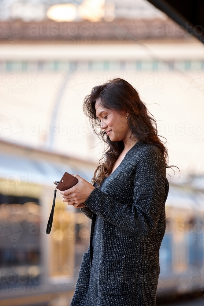 Asian woman waiting at train station using mobile phone - Australian Stock Image