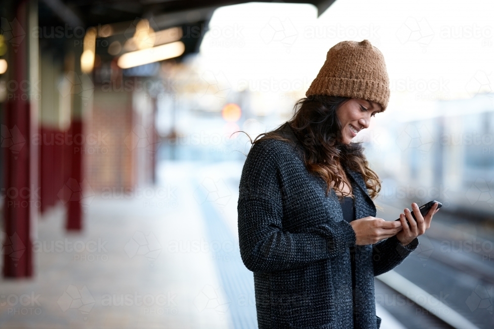 Asian woman waiting at train station using mobile phone - Australian Stock Image