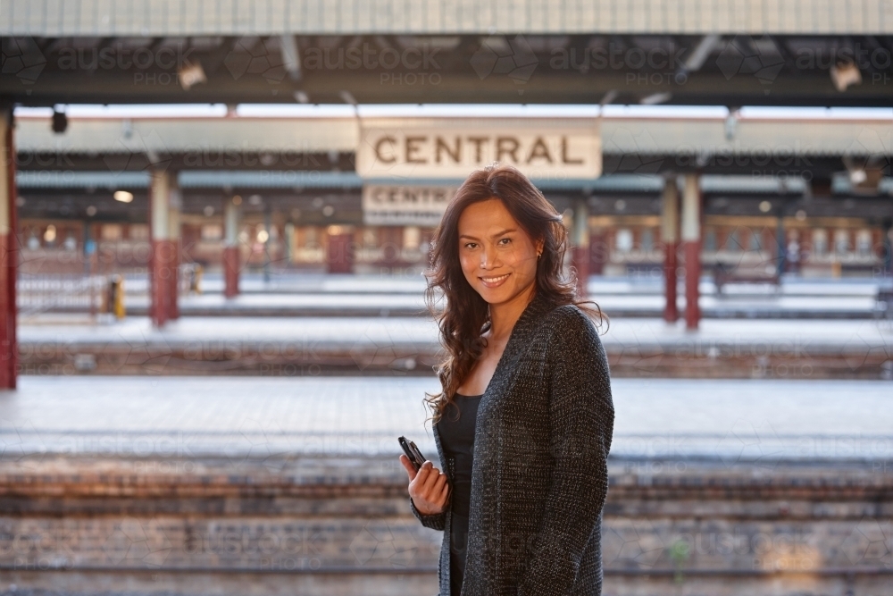 Asian woman waiting at train station with mobile phone - Australian Stock Image