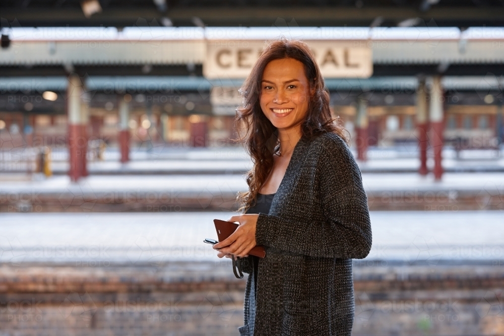 Asian woman waiting at train station with mobile phone - Australian Stock Image