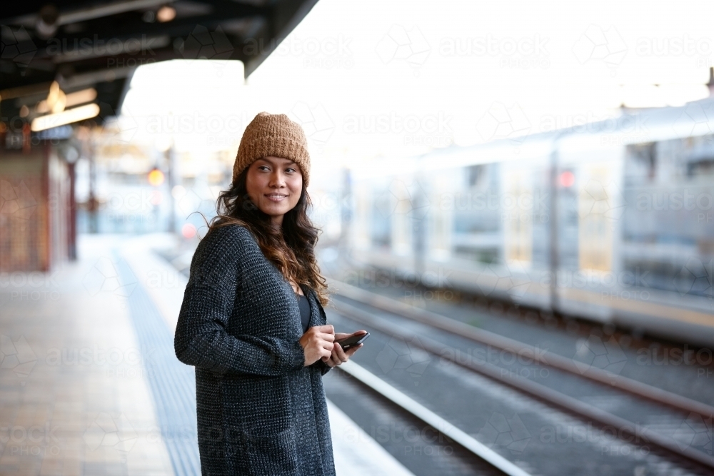 Asian woman waiting at train station with mobile phone - Australian Stock Image