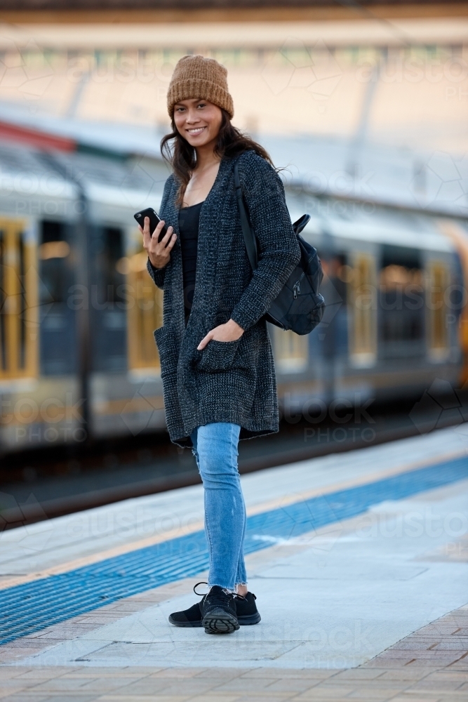 Asian woman waiting at train station with mobile phone - Australian Stock Image