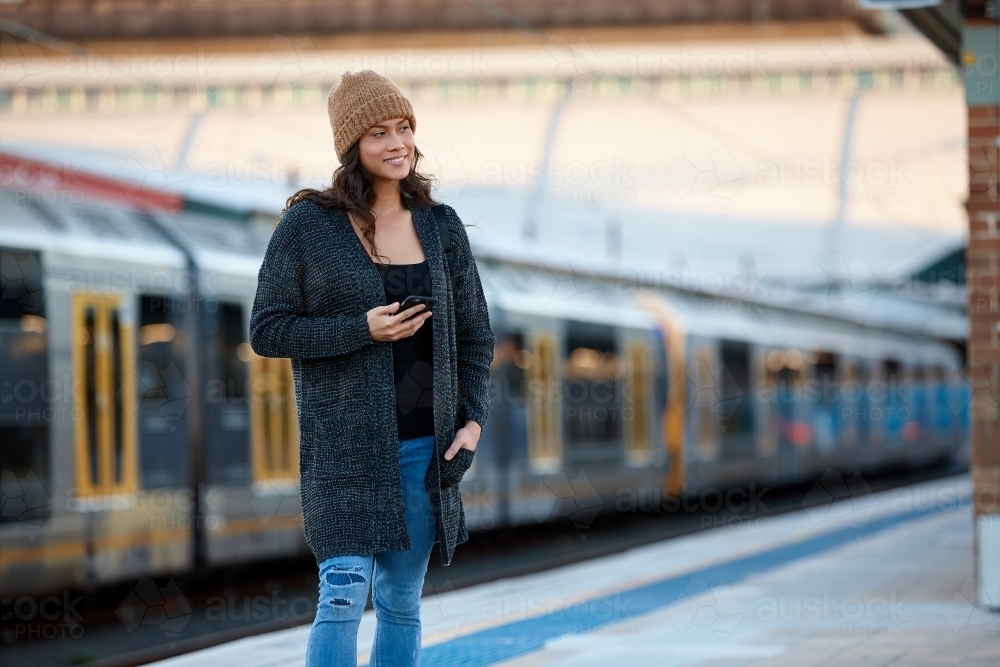 Asian woman waiting at train station with mobile phone - Australian Stock Image